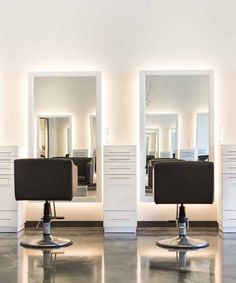 two salon chairs sitting in front of mirrors with lights on the wall above them and below them