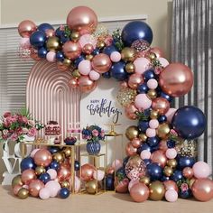 an arch made out of balloons and other decorations on a table in front of a window