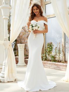 a woman in a white wedding dress holding a bouquet and standing next to a window