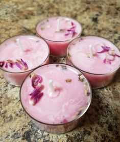 four candles with flowers in them sitting on a counter top next to a marble surface