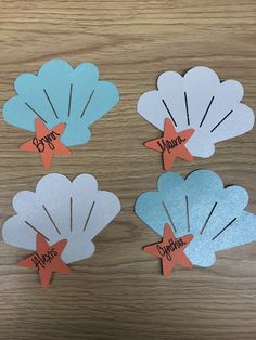 four seashells with name tags on them sitting on a wooden table next to each other