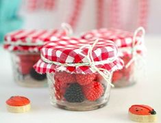 three small jars filled with red and black berries on top of a white tablecloth