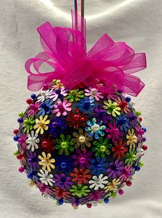 a colorful ornament hanging on a white wall with a pink ribbon and bow