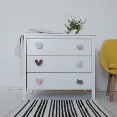 a white chest of drawers sitting next to a yellow chair and potted plant on top of it