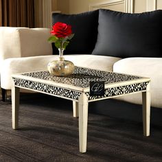 a coffee table with a flower on it in front of a white couch and black pillows