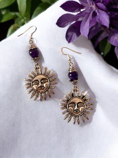 These whimsical silver sun face charm earrings call back to 90s whimsigoth fashion incorporating a smiling sun and the purple amethyst stone. The smiling sun charm is made of a silver alloy and is connected to the amethyst stone using hypoallergenic jewelry wire. The amethyst stone is purple in color and is measuring at 8mm. It has too ornate silver decorative holders on either side to give the stone more interest. These earring feature hypoallergenic Sterling Silver 925 ear wires. The drop length of these earrings is 2" with a 1" measurement at its widest.  Amethyst is stone that provides grounding energy and protection in all aspects of life. It is often associated with lucidity/sobriety and purity. As with all of my jewelry, when purchased an information card will be included to provide Whimsigoth Fashion, 90s Whimsigoth, Sun Celestial, Witchy Earrings, Smiling Sun, Grounding Energy, Sun Charm, Sun Face, Purple And Silver