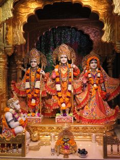 statues of hindu deities in front of a shrine with gold and orange decorations on the walls