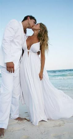 a man and woman standing on the beach in front of the ocean wearing white outfits