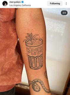 a person with a tattoo on their arm holding a glass filled with water and plants