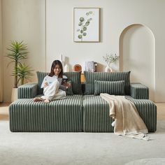 a woman sitting on top of a green couch in a living room next to a white rug