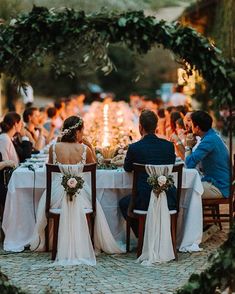 a group of people sitting at a table with white cloths and flowers in front of them