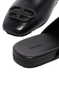 These black Balenciaga BB logo leather slipper shoes feature a square toe, slip-on design, flat sole and BB logo plaque.Calfskin leather with leather soleRubber tap heelMatte black-tone BB logo detail Composition: Leather 100%Lining Composition: Leather 100%Sole Composition: Leather 100% Fits true to sizeMade in Italy Black Calf Leather Slip-ons With Removable Insole, Luxury Leather Flat Slip-ons, Leather Slip-ons With Square Toe And Rubber Sole, Luxury Flat Slip-ons With Rubber Sole, Business Slip-ons With Leather Sole, Leather Mules With Branded Heel For Business, Formal Flat Mules With Textured Sole, Leather Square Toe Mules With Rubber Sole, Black Square-toe Calf Leather Loafers