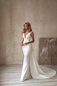 a woman in a white wedding dress standing on a wooden floor with her hands behind her back