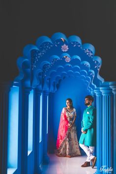 a man and woman standing in front of an archway with blue arches on either side