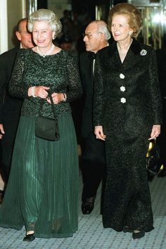 two women in green dresses walking next to other people wearing black suits and holding hands