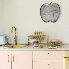 a kitchen with an apple shaped wall hanging above the sink and dishes on the counter