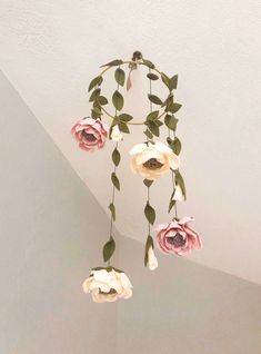 a white and pink flower mobile hanging from the ceiling with green leaves on it's end