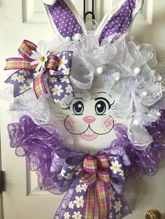 an easter bunny wreath is hanging on the front door with purple and white flowers around it