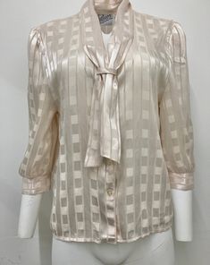 This is an authentic 1980s blouse in a cream jacquard fabric by Peepers of London. Details include a V neck with tie that hangs through a loop at the front, lightly puffed shoulders with small shoulder pads, 3/4 length sleeve and fine gold lamé stripes, running vertically down the jacquard check pattern. Size and fit: This blouse measures 22 inches across and hangs straight down so would best fit a UK size 12-16. The back measures 24 inches from collar to hem. Condition: This blouse is in very g Vintage Silk Blouse For Formal Occasion, Vintage Tie Neck Office Top, Vintage Office Tie Neck Top, Vintage Tie Neck Top For Office, Cream Blouse For Formal Occasions In Fall, Vintage Tie Neck Blouse For Work, Vintage Tie Neck Tops For Formal Occasions, Vintage Beige Blouse For Party, Vintage Beige Party Blouse