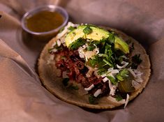 a tortilla with meat and vegetables on it next to a cup of sauce