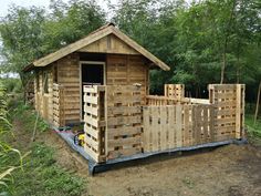 a building made out of wooden pallets in the middle of some trees and grass