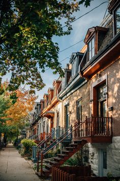 a row of brick townhouses with stairs leading up to the second story and trees lining the sidewalk