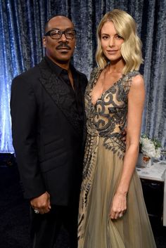 a man and woman standing next to each other in front of a curtained wall