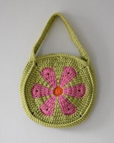 a crocheted purse with a pink flower on the front and green bottom, hanging from a white wall