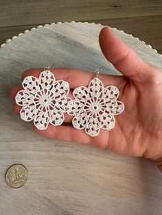 a hand holding three white crocheted flower earrings