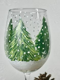 a painted wine glass sitting on top of a table next to a pine tree and snow