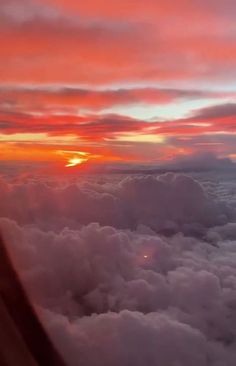 the sun is setting over some clouds from an airplane window as it flies through the sky