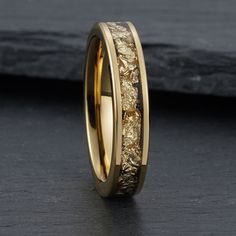 a wedding band with gold leaves inlaying the center, on a black surface