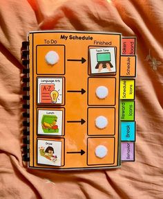 an orange notebook with pictures on it sitting on top of a bed covered in pink sheets