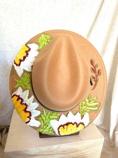 This one of a kind, hand painted, textured floral fedora is the perfect walking art piece. Each hat is uniquely crafted and perfect for any occasion.  This tan fedora is crafted with white, yellow, deep red flowers, and bright green leaves with metallic gold accents. These island treasures are shipped straight to you from the Hawaiian island of Oahu. (Hats are water resistant. Keep out of heavy rain. Spot clean only) Hand Painted Brimmed Hats For Spring, Artisan Short Brim Hat For Spring, Artistic Fedora Hat For Spring, Artisan Felt Hat For Summer Rodeo, Artisan Wide Brim Fedora For Spring, Artisan Wide Brim Spring Hats, Artistic Short Brim Hat For Spring, Spring Artistic Fedora Hat, Artistic Fedora With Short Brim For Spring