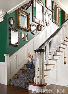 a child sitting on the stairs in front of a staircase with mirrors and framed pictures