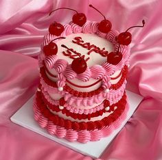 a pink and white cake with cherries on top is sitting on a pink cloth