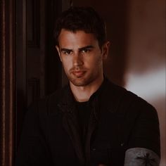 a young man in a black shirt is looking at the camera while standing next to a door