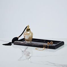 a black tray with a white and gold vase sitting on top of it next to a pair of earrings