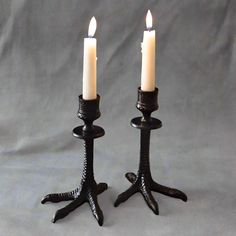 two black candlesticks sitting on top of each other with one candle lit in the middle