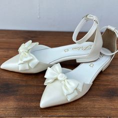 a pair of white wedding shoes with bows on the toes and heels are sitting on a wooden table