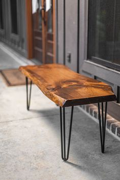 a wooden bench sitting on top of a sidewalk next to a building with black hairpin legs