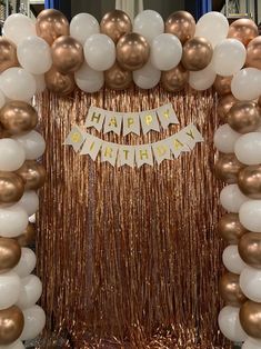 a gold and white balloon arch with happy birthday banner on the top, surrounded by balloons