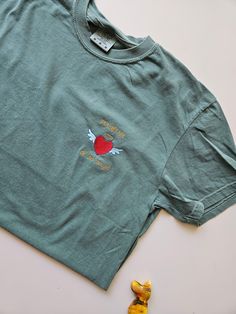 a green t - shirt with an apple on the chest and two yellow rubber ducks next to it