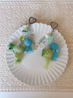 three little elephants are on a paper plate with some charms hanging from it's sides