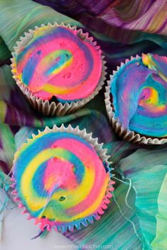 three cupcakes with rainbow icing sitting on top of green leafy paper