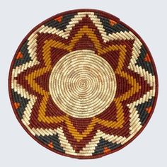 a red, yellow and green woven basket on a white surface with an intricate design in the center