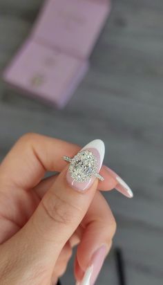 a woman's hand holding a diamond ring on top of her finger with white nails