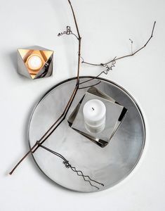 a candle is sitting on top of a round metal plate with branches in the background