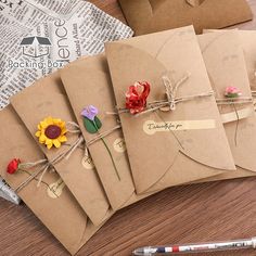 four brown envelopes tied with twine and decorated with paper flowers, sitting on a wooden table