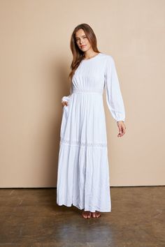 a woman wearing a white dress standing in front of a beige wall with her hands on her hips